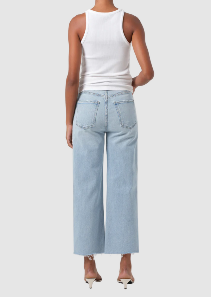 Person wearing a white tank top and light blue wide-leg jeans on a plain background