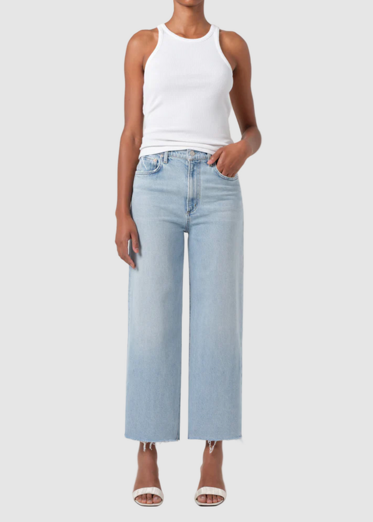 Person wearing a white tank top and light blue jeans on a plain background